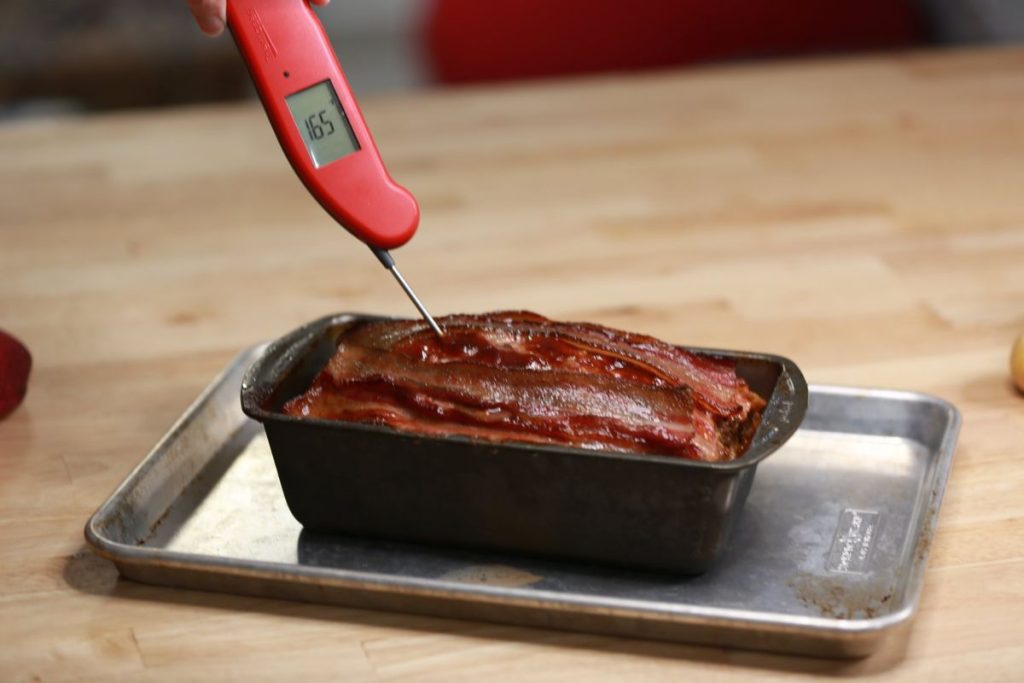 Instant-read thermometer reading 165°F in a bacon-topped BBQ meatloaf